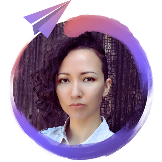 A picture of author and games writer Lisa Hosokawa, a mixed-Japanese and White nonbinary person with a shoulder-length, curly sidecut, dark eyes, and light beige skin, standing in front of dark-brown wooden siding.